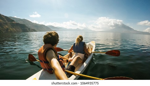 Outdoor Nature Selfie Of Young Lovely Couple Canoeing Kayaking On Sunny Day On Lake Sea With Mountain View Background. Best Friends Enjoying And Having Fun Together On Kayak In Vacation Holiday Trip.