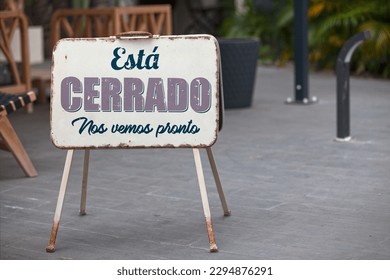 Outdoor open sign with written in it in Spanish "Está cerrado. Nos vemos pronto" meaning in English "It's closed. See you soon".