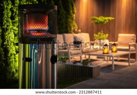 Outdoor Patio Propane Gas Heater For Cold Evenings in Garden Area. Burning Heater in Front of Outdoor Relaxing Area During Night Time.