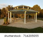 an outdoor pavillion with picnic tables, grill, and trash can