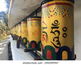 Outdoor perspective shot of a row of yellow Tibetan Buddhist prayer wheels decorated with colourful symbols meaning “Praise to the Jewel in the Lotus” on the path around the Dalai Lama temple, India