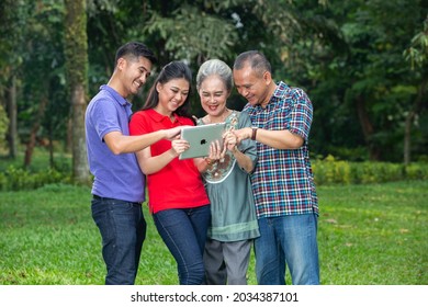 
Outdoor Photo Session Of A Happy Family Where Their Children Are Grown Up Holding Their Ipad And Communicating With Their Family In Another City, Jakarta-Indonesia.June 11 2014