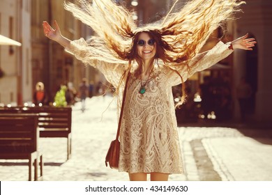 Outdoor Photo Of Young Beautiful Happy Smiling Woman Playing With Her Long Hair. Model Wearing Stylish Summer Dress. Girl Looking At Camera. Female Fashion. Sunny Day. City Lifestyle. Waist Up. Toned