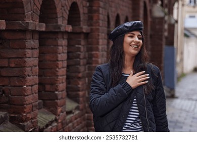 Outdoor photography, rain fashion, city woman. In rain, stylish woman wearing black jacket and white pants strolls by brick wall, smiling naturally. - Powered by Shutterstock