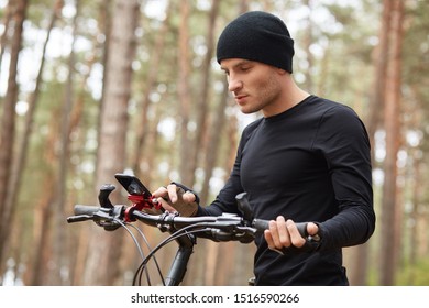 Outdoor picture og attractive young guy holding mobile phone in hands, male traveling on bike through forest, finding right way via smartphone, internrt or navigator, spending free time in open air. - Powered by Shutterstock