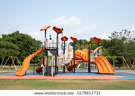 The outdoor playground in the daytime has a backdrop of green trees and blue skies.