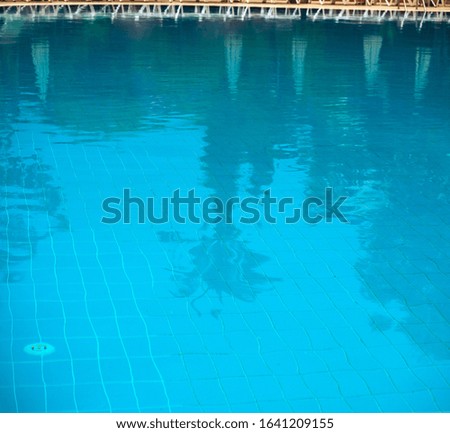 Outdoor pool. Through the water you can see the bottom of the pool. Palm trees and sun umbrellas are reflected in the water. Transparent water background with reflections.