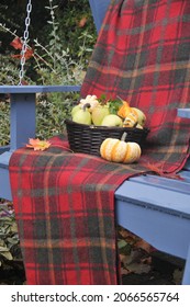 Outdoor Porch Swing In Garden Setting With Harvest Basket Of Apples And Cozy Fall Blanket.