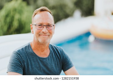 Outdoor Portrait Of 50 Year Old Man Resting By The Pool, Wearing Blue T-shirt And Glasses