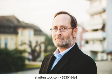 Outdoor Portrait Of 50 Year Old Man Wearing Black Coat And Eyeglasses