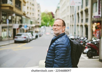Outdoor portrait of 55-60 year old man wearing blue jacket and backpack, looking back over the shoulder - Shutterstock ID 2254688097
