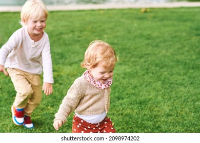 Outdoor portrait of adorable happy children playing together, running after each other, siblings love