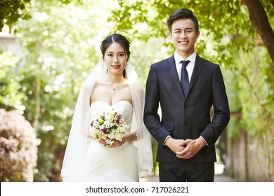 outdoor portrait of asian bride and groom looking at camera smiling.