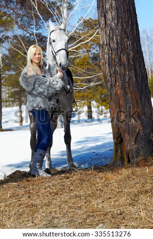outdoor portrait of beautiful blonde girl in furs with pale horse in sunny winter forest