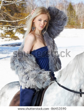 outdoor portrait of beautiful blonde girl sitting on pale horse in sunny winter forest