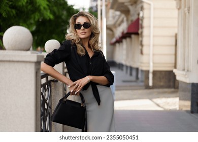 Outdoor portrait of beautiful elegant blond woman with perfect wavy hairs  holding luxury hand bag. Fashion acsessories, sunglasses. - Powered by Shutterstock