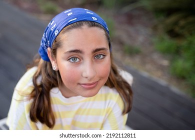 Outdoor portrait of beautiful happy teen girl with rosy cheeks. Young woman with beautiful big green eyes. Smiling face. Eye contact. Stylish image, blue bandana. Sunset. Beauty, embarrassment concept