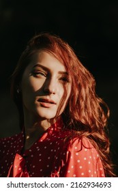 Outdoor portrait of a beautiful young adult woman with full lips green eyes red hair and dressed in red country road shirt with white dots