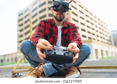 Outdoor portrait of casually dressed male fpv pilot operating multicopter drone using goggles nad remote controller. Focus is on the hands.