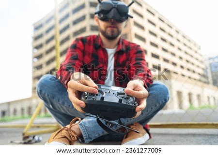 Outdoor portrait of casually dressed male fpv pilot operating multicopter drone using goggles nad remote controller. Focus is on the hands.