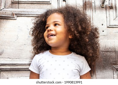 Outdoor Portrait Of A Curly African American Girl On A Background Of Old Wooden Door.