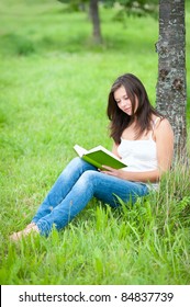 Outdoor Portrait Of A Cute Teen Sitting Under A Tree And Reading A Book