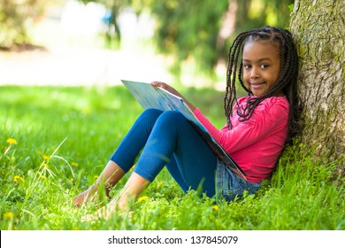 Outdoor portrait of a cute young black little  girl reading a book - African people