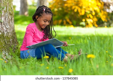 Outdoor portrait of a cute young black little  girl reading a book - African people