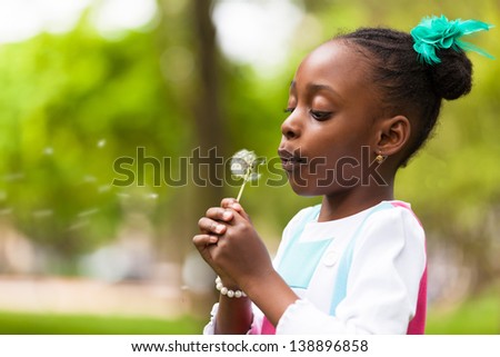 Outdoor portrait of a cute young black girl blowing a dandelion flower - African people