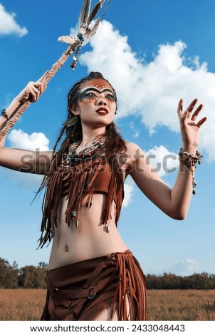Outdoor portrait of the cute young shamaness (witch doctor) with staff. Beautiful shaman (enchantress) making ritual. Sorceress in the field