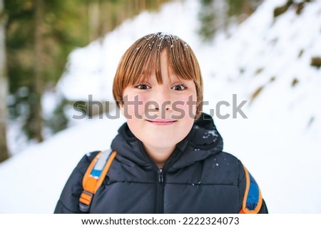 Outdoor portrait of cuty kid hiking in winter forest, young boy wearing backback hiking in mountains