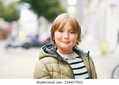 Outdoor Portrait Of Handsome 10 Year Old Kid Boy, Wearing Warm Jacket, Looking Straight At Camera, Posing On City Street