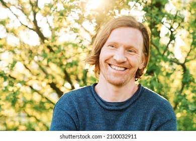 Outdoor Portrait Of Handsome 35 - 40 Year Old Man With Red Hair, Posing In Green Sunny Park, Wearing Blue Pullover