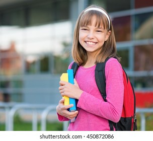 Outdoor portrait of happy girl 10-11 year old with book and backpack. Back to school concept.