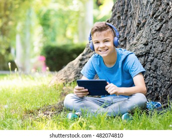 Outdoor portrait of happy teen boy 12-14 year old in headphones with tablet. Schoolboy watching media content in a tablet at park. - Powered by Shutterstock