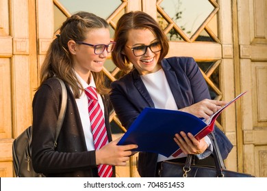 Outdoor Portrait Of A High School Teacher With A Schoolgirl Near The Front Door Of The School.