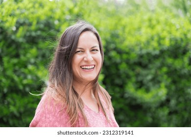 Outdoor portrait of a laughing 45 year old woman with windblown brown hair looking at the camera in the park on a sunny day. Confidence and tranquility of a mature woman. Happiness, lifestyle. - Powered by Shutterstock