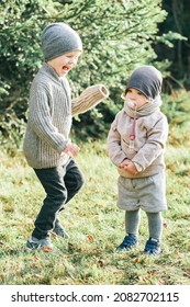 Outdoor Portrait Of Little Preschool Brother Trying To Cheer Up Shy Toddler Sister