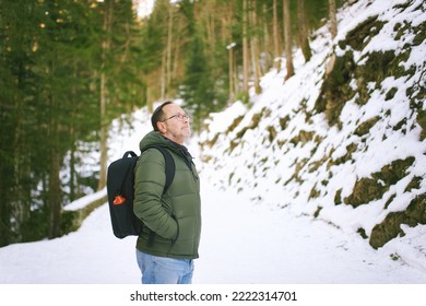 Outdoor Portrait Of Middle Age 55 - 60 Year Old Man Hiking In Winter Forest, Wearing Warm Jacket And Black Backpack