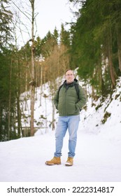 Outdoor Portrait Of Middle Age 55 - 60 Year Old Man Hiking In Winter Forest, Wearing Warm Jacket And Black Backpack