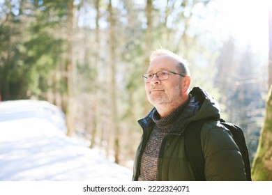 Outdoor Portrait Of Middle Age 55 - 60 Year Old Man Hiking In Winter Forest, Wearing Warm Jacket And Black Backpack