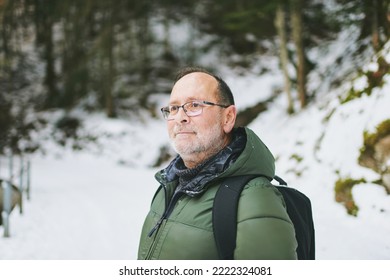 Outdoor Portrait Of Middle Age 55 - 60 Year Old Man Hiking In Winter Forest, Wearing Warm Jacket And Black Backpack