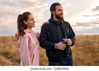 Outdoor portrait of positive couple in nature countryside relaxing before or after jogging. attractive female and male in hoodie laughing, talking. wellbeing, healthy lifestyle, human emotions - Powered by Shutterstock