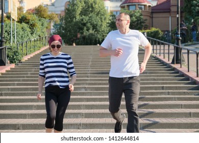 Outdoor Portrait Of Running Mature Couple. Man And Woman Of 40 Years Old Running Up The Stairs. Active Sports Healthy Lifestyle Of Age People