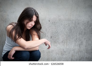 Outdoor portrait of a sad teenage girl looking thoughtful about troubles in front of a gray wall