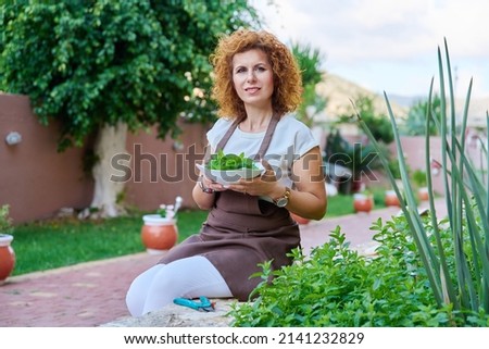 Outdoor portrait of smiling female cook in an apron with plate of fresh mint