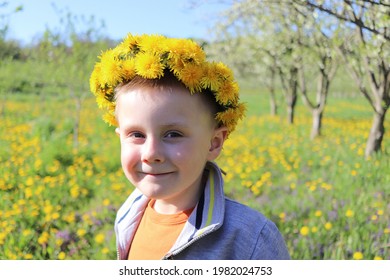 Outdoor Portrait Of A Smiling Little Boy With A Dandelion Crown On His Head.