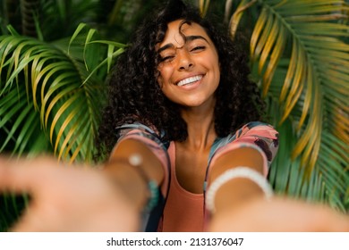 Outdoor  portrait of smiling lovely woman with curly hairs posing over tropical trees and palm leaves. 