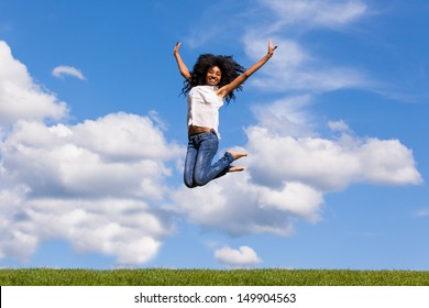 Outdoor portrait of a smiling teenage black girl jumping over a blue sky - African people