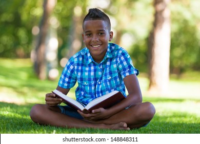 Outdoor portrait of student black boy reading a book - African people